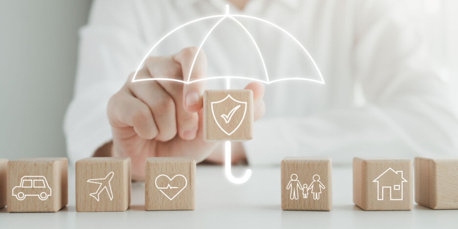 Insurance concept. Protection against a possible eventuality. House, Car, Family, travel and Health on wooden block and Hand holding security icon cover by umbrella icon for life assurance concept.