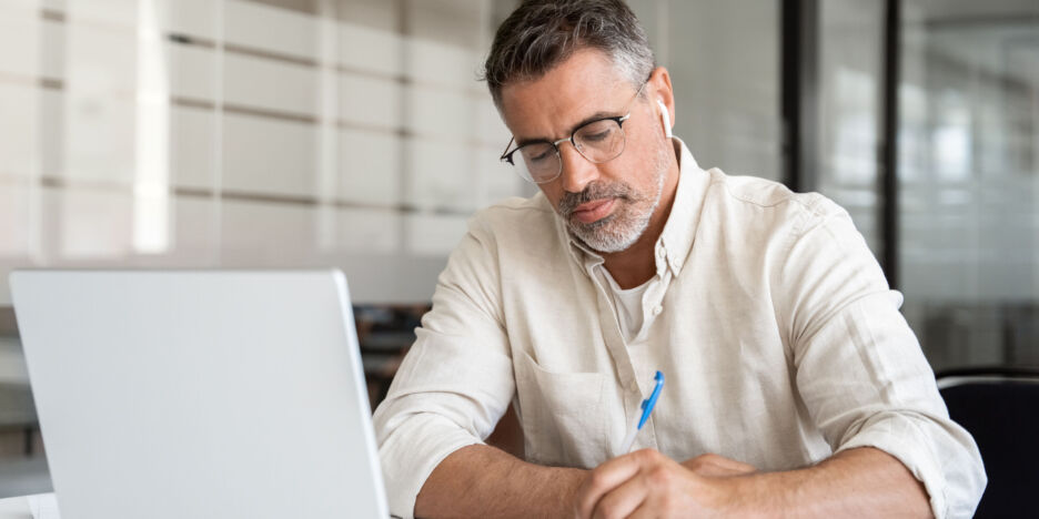Focused middle-age Hispanic man using laptop computer for business studying, watch online virtual webinar training meeting, video call, make notes. Mature Latin businessman work in office, close-up.