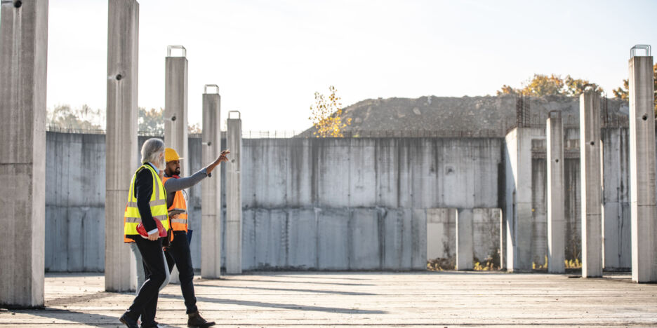 Mid distance side view of African foreman in early 30s doing construction site walk-through with mature Caucasian project managers.