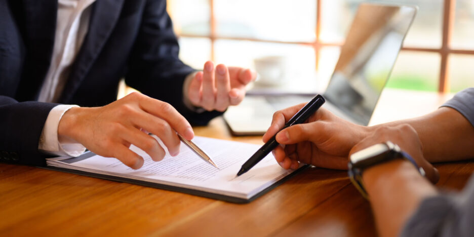 Closeup lawyer or insurance agent pointing at contract showing male client where to signature sign.